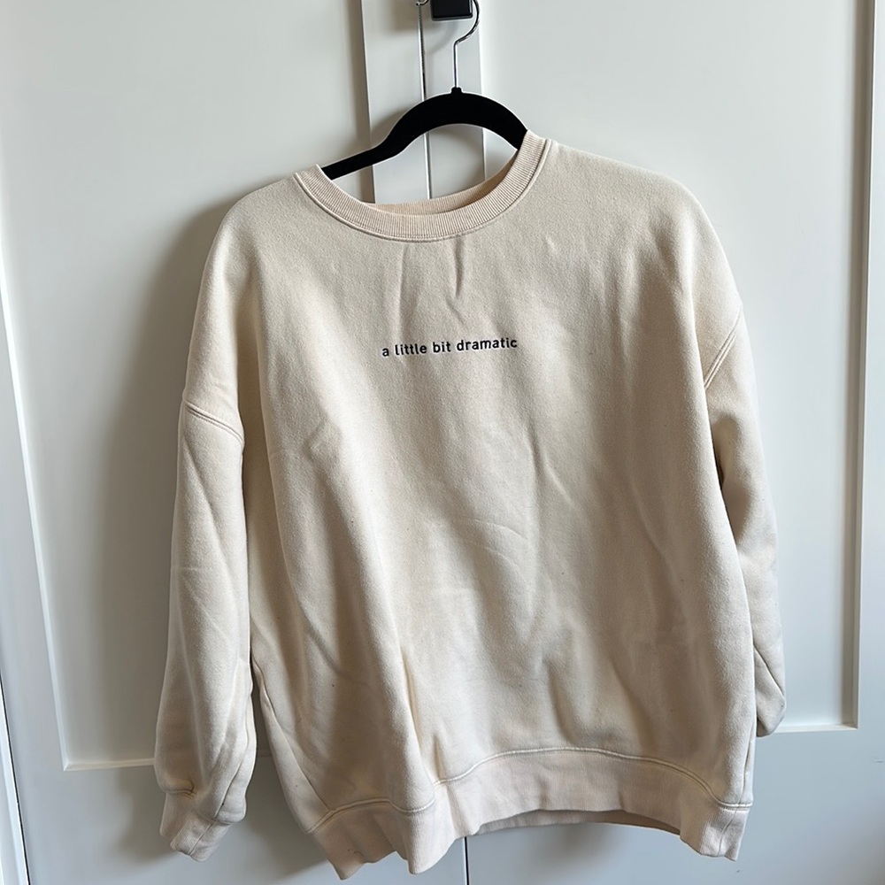 Light cream crewneck. Text: “a little bit dramatic”. Good condition.